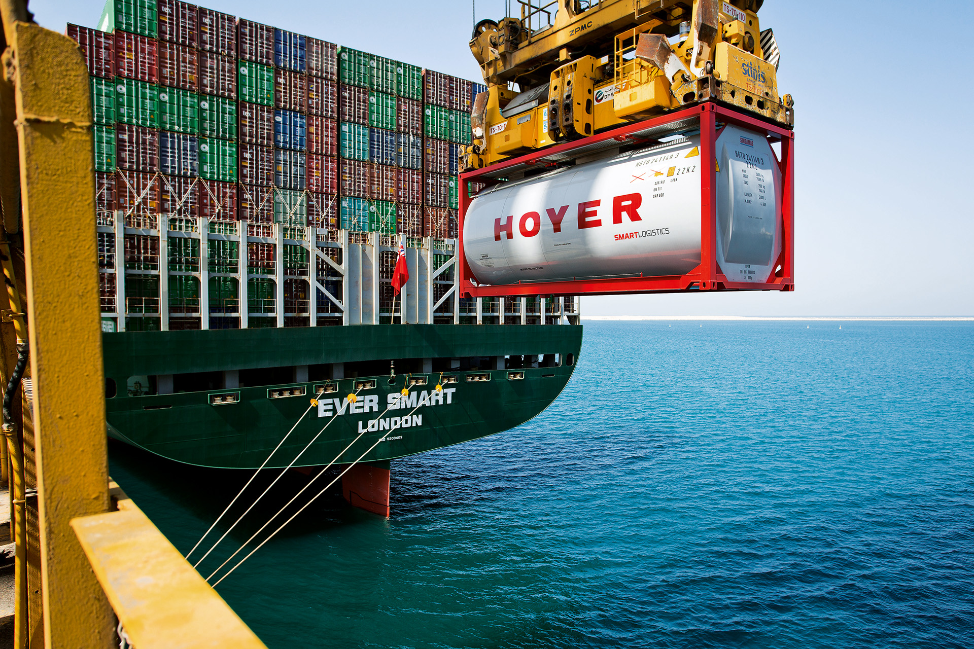 HOYER Container smart logistics an einem Kran ueber dem Meer am Hafen mit Schiff im Hintergrund