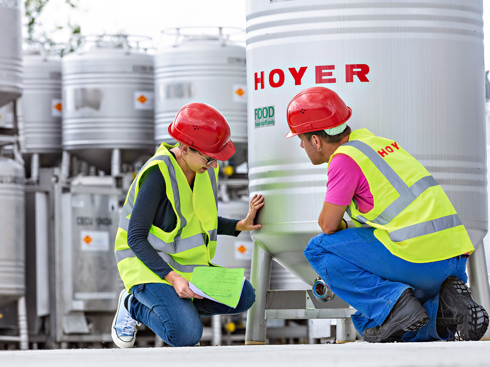 Two HOYER employees kneel in front of the bottom outlet of an IBC 