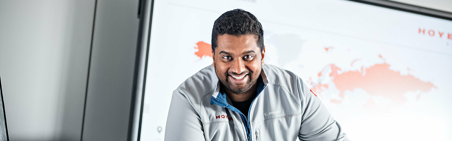 Employee in HOYER jacket stands smiling leaning against a table