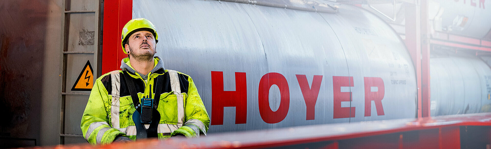 HOYER employee in front of HOYER tankcontainers, lifts tankcontainer with crane