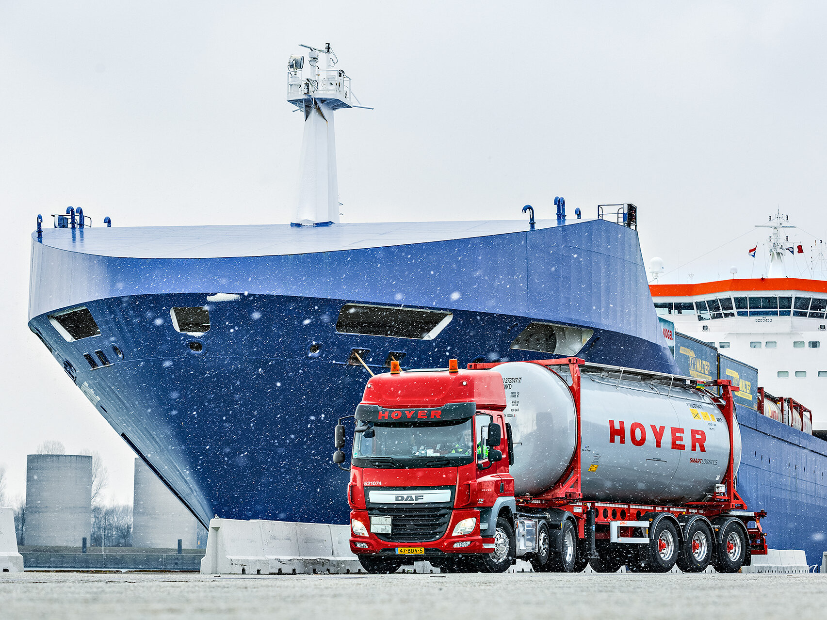 HOYER Lkw mit Chemie-Tankcontainer smart logistics vor einem Schiff. Es schneit.