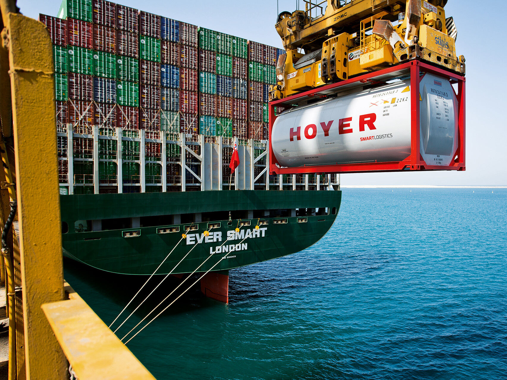 HOYER tankcontainer smart logistics on a crane over the sea in front of a container ship