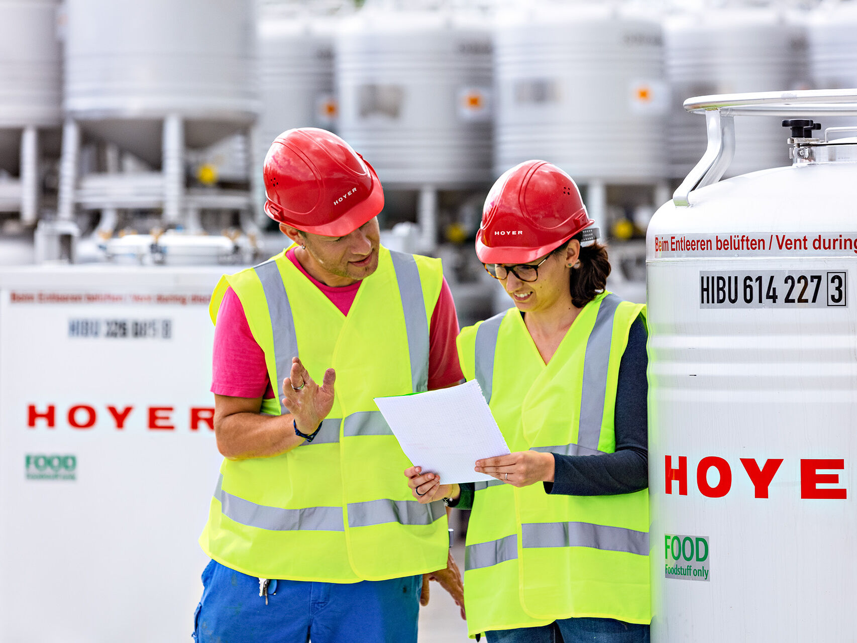 Two HOYER employees in front of a Food IBC and look at a document 