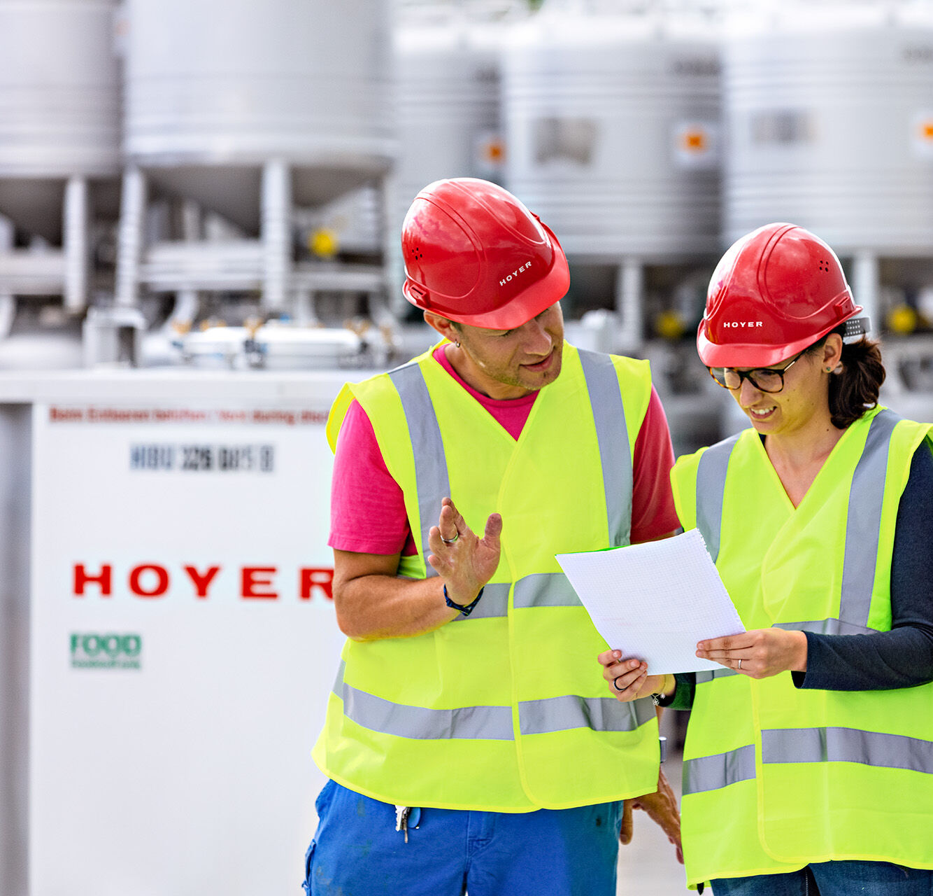 Zwei HOYER Mitarbeiter stehen zwischen zwei IBC und schauen auf ein Dokument 