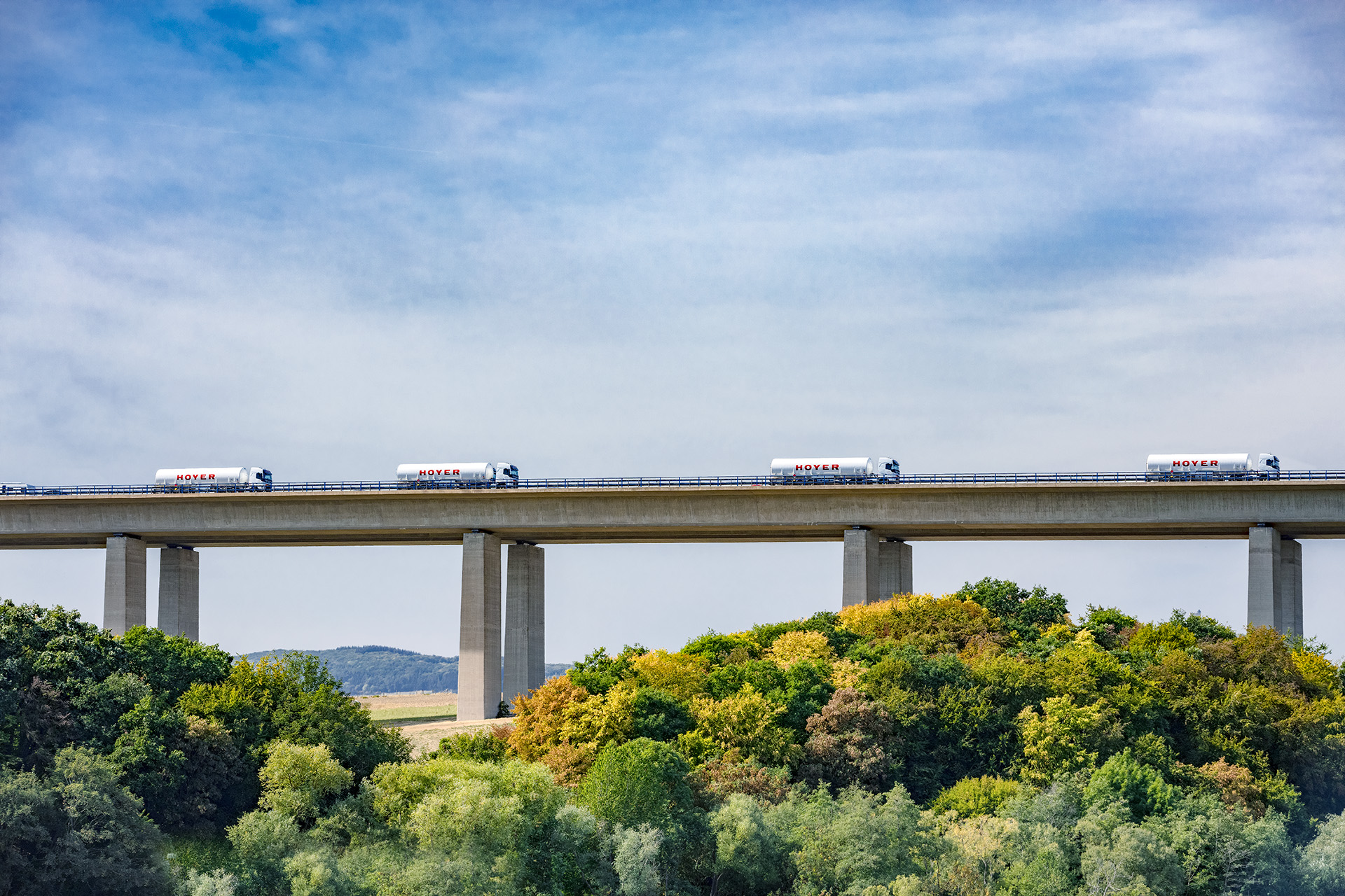 Four white HOYER trucks with gas container on a bridge