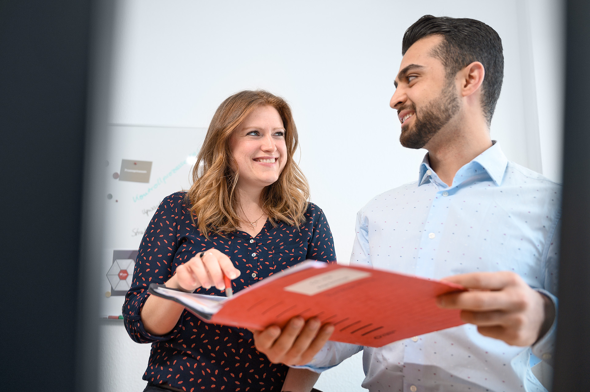 Two employees look at each other, holding a document folder